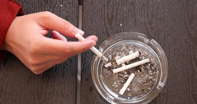 Woman flicking ash from cigarette into ashtray at wooden table, top view