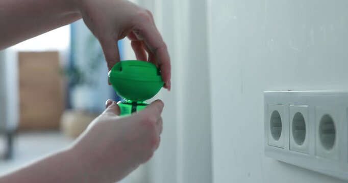 Woman plugging electric mosquito repeller with liquid refill at home, closeup