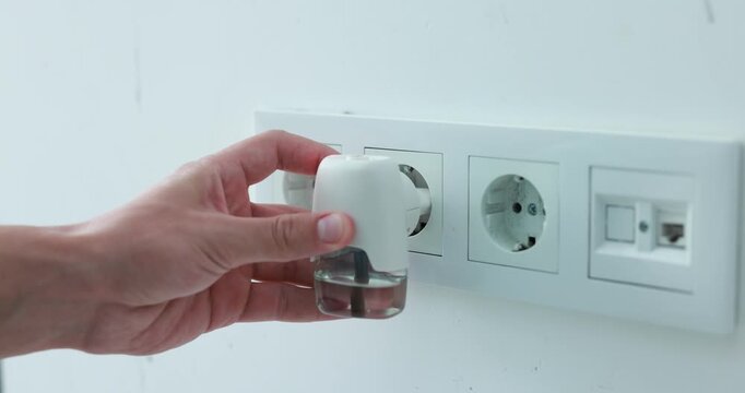 Man plugging in electric mosquito repeller with liquid refill at home, closeup