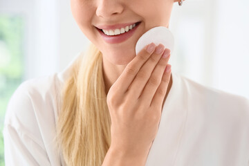 Smiling young woman with blonde hair applying facial toner with a cotton pad for daily skincare routine © Pixel-Shot