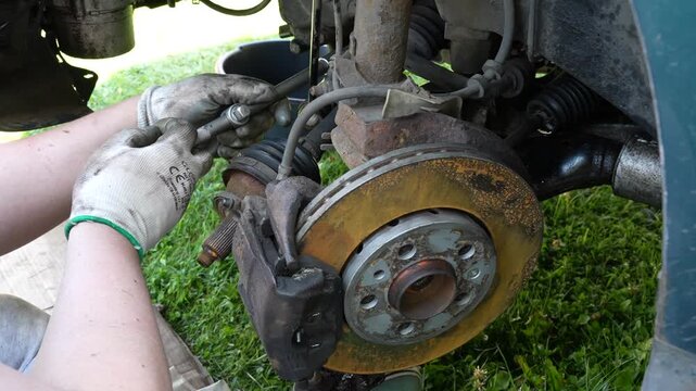 Mechanic wearing protective gloves repairing car suspension and loosening bolts with a ratchet wrench outdoors