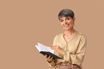 Naklejka premium Smiling mature woman with short gray hair holding an open book, education and learning concept, isolated on a brown background