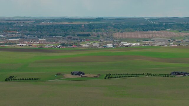 High altitude drone shot of an isolated country home under construction with planted windbreak trees on an open midwestern landscape, sitting outside town limits under a cloudy sky.