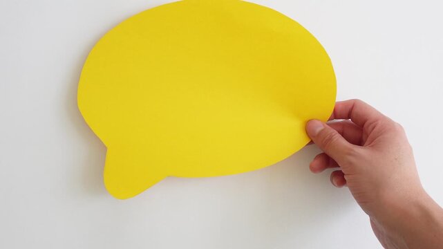 Hand holds bright yellow speech bubble. Clean white background. Ideal for communication or messaging themes.