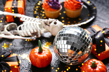 Fototapeta premium Halloween party decorations with disco ball, skeleton, cupcakes, pumpkins, and gift boxes on a dark background