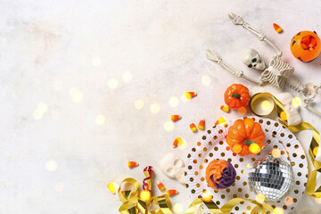 Fototapeta premium Halloween party flat lay with skeleton candy corn pumpkin decorations and cupcakes on a white background with bokeh lights