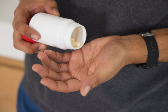 Man pouring beige capsules from white plastic pill bottle into open palm at home