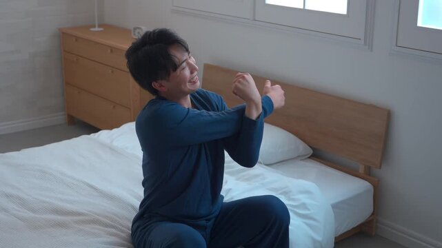 朝のベッドで腕をほぐすストレッチをする男性