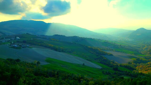 Spiritual aerial push-in shot near Santa Vittoria in Matenano, heavenly sunlight shining through the clouds and the majestic Sibillini Mountains, their hazy ridges imbued with a mysterious atmosphere
