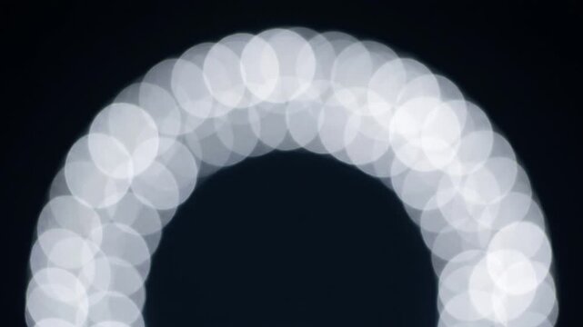 見えないU字磁石の磁力線に沿って銀色の円形ボケがアーチを描く、抽象的な光のトポロジー映像。