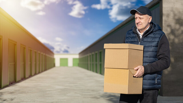 Self storage. Customer carries cardboard boxes at a self storage facility while moving personal belongings, using rental storage units for relocation and organization.