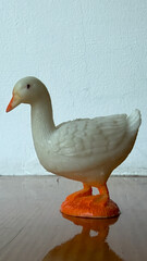 A goose figurine standing on a wooden surface against a clean white wall, decorative animal statuette. © Анна Трегубова