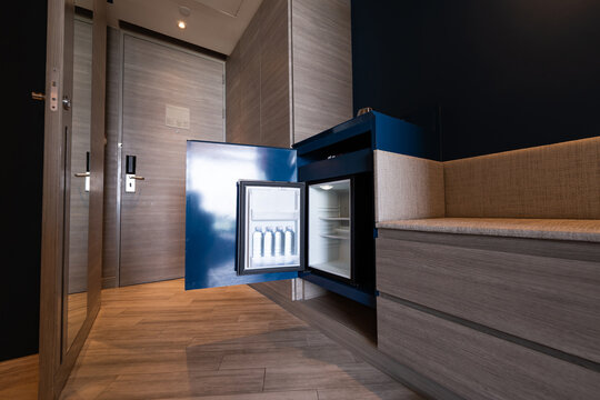 Hotel black minibar refrigerator guest room features a mini fridge neatly placed beneath a blue wooden desk, functional workspace with convenient in contemporary room.