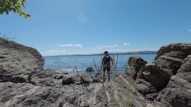 Man walking down rocky coast dropping backpack to contemplate fjord water
