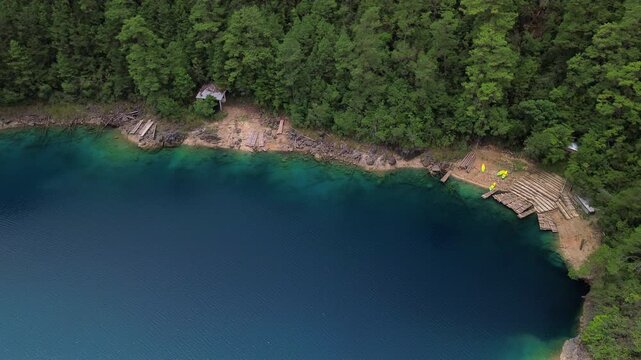 Static top-down aerial drone shot of turquoise lake shore with wooden docks and dense pine forest at Montebello Lakes, Chiapas, Mexico.