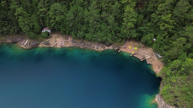 Static top-down aerial drone shot of turquoise lake shore with wooden docks and dense pine forest at Montebello Lakes, Chiapas, Mexico.
