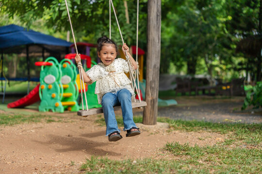happy preschool child girl swinging on a wooden swing in a playground.
