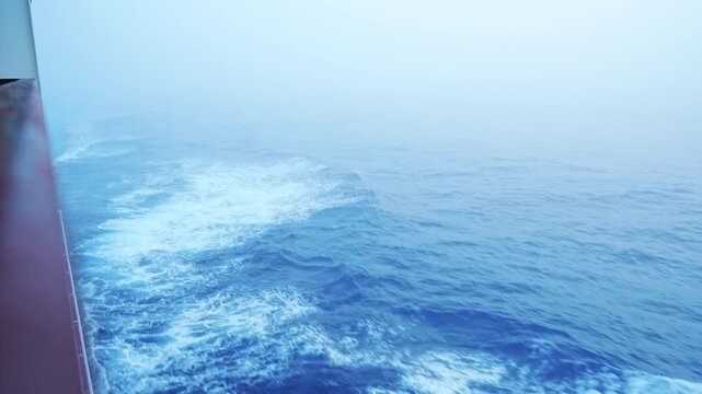View from the stern of a ship sailing through a misty ocean covered in morning fog