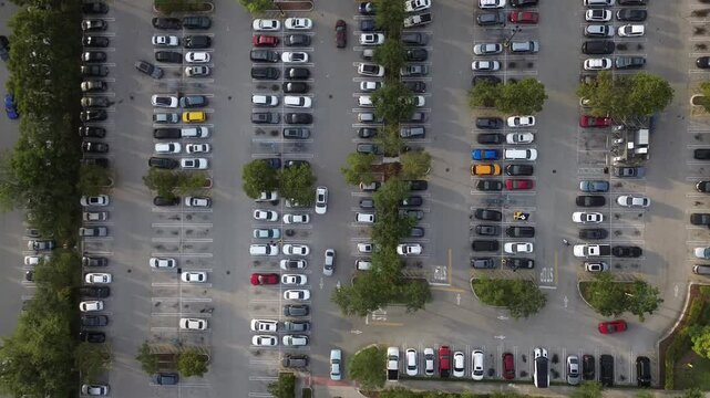 Drone hovers over a crowded parking lot as cars and pedestrians move between the rows at sunset