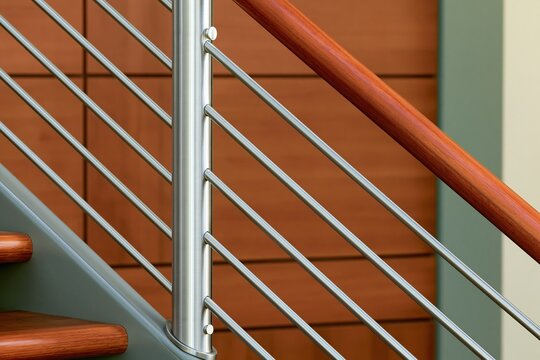 Close up detail of modern mixed material staircase railing combining brushed stainless steel vertical bars and warm natural wood handrail for contemporary residential interior