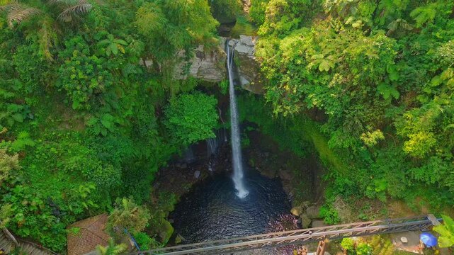 Aerial view of Curug Telu waterfall surrounded by lush tropical forest and rocky cliffs in Baturaden, Jawa Tengah, Indonesia.
