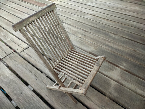 Angled view of a rustic wooden folding deck lounger chair set on matching outdoor teak patio flooring. Ideal for garden furniture and summer relaxation