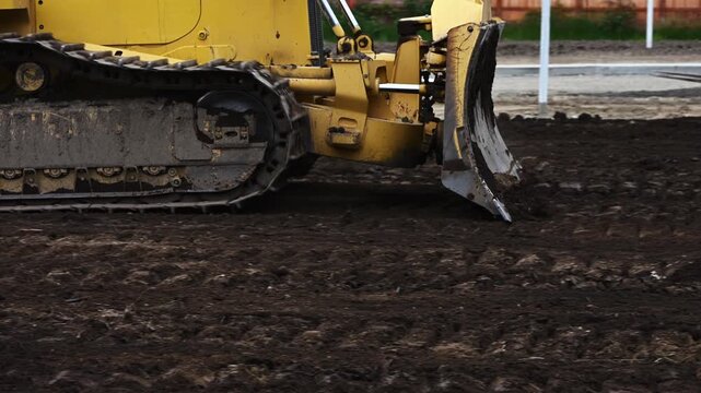 Crawler bulldozer moving dirt, leveling and leveling ground in new residential development, heavy blade moving earth, summer construction work in progress

