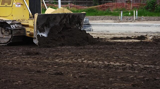 Crawler bulldozer moving dirt, leveling and leveling ground in new residential development, heavy blade moving earth, summer construction work in progress
