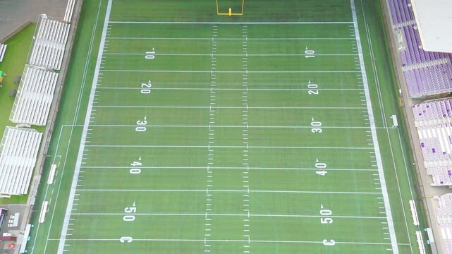 Bird's-eye view of empty football field turf with yard lines and bleachers