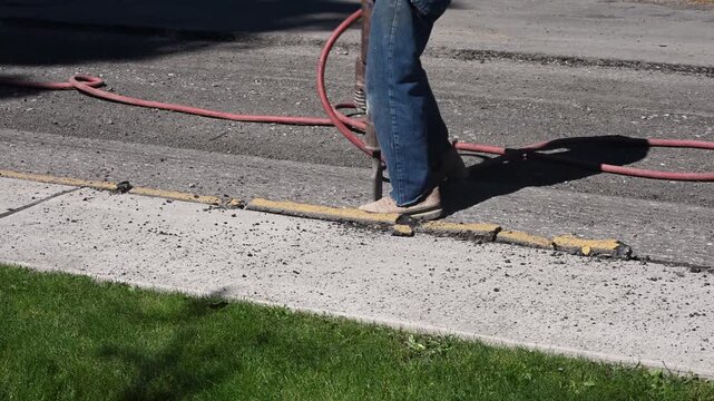 Construction worker using jack hammer to break up old asphalt as part of road repaving infrastructure project
