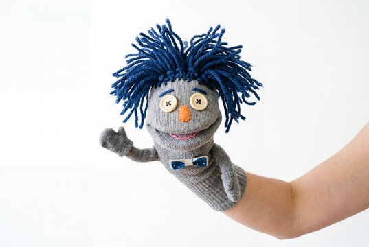 Handmade grey sock puppet with blue yarn hair on a human hand