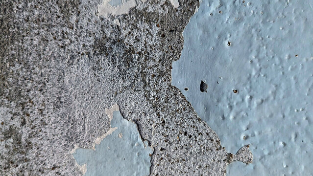 Peeling light blue paint on a rough concrete wall texture.