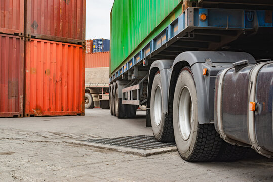 Detail of semi-truck tires loaded with heavy commercial shipping containers at terminal, real image, not AI generated.