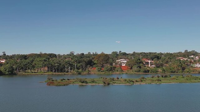 Aircraft flying above Lake Paranoa in Brasilia, Federal District, Brazil, revealing the freshwater reservoir, wooded shoreline, residential district and small vegetated islands, drone tracking.