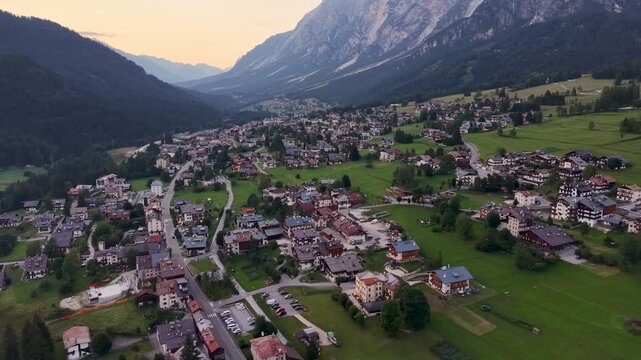 Drone view above San Vito di Cadore at sunset with the alpine village surrounded by the dramatic peaks of the Dolomites, Italy