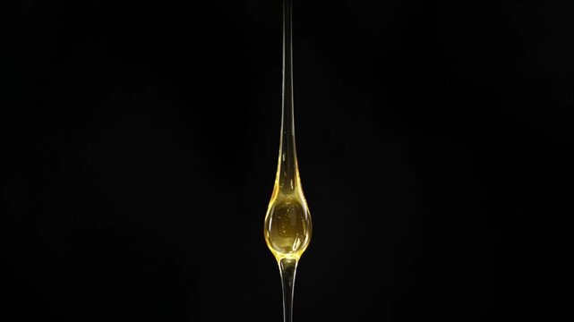 Cinematic single object macro background drop of golden honey and liquid oil against dark background creating dramatic minimal mood vertical motion gravity fluid texture shimmer droplet suspended