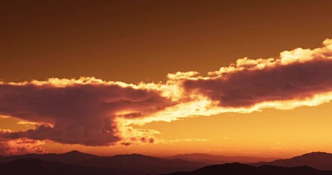 Breathtaking sunset landscape featuring vibrant orange clouds drifting over distant mountain silhouettes during the golden hour of twilight