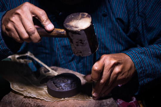 Detailed view of craftsman hand holding chisel tool and wooden mallet while making leather shadow puppet