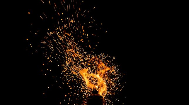 Bright orange fire sparks flying from a torch against a black background