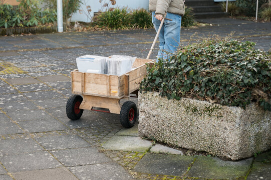 Wooden handcart loaded with bundled newspapers being pulled through residential neighborhood, local newspaper distribution, print media delivery and community logistics concept