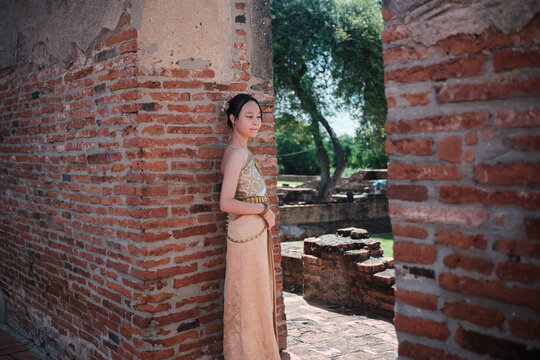 One Asian teenage girl dressed in traditional Thai outfit standing at old town brick wall, holiday travel in Ayutthaya historical park, Southeast Asia, ancient ruins heritage,  tourist destination.