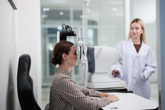 White female patient eye exam with phoropter equipment, vision and eyesight improvement by expert optometrist woman, diagnostic for eyeglasses lens, professional technology services in optical clinic.