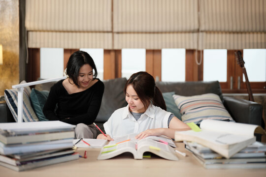 Two Asian teenage girls learning tutorials at home together, reading textbooks, writing notes, self-tutorial exams, preparation for back to school, Homeschooling study, knowledge education lifestyle.