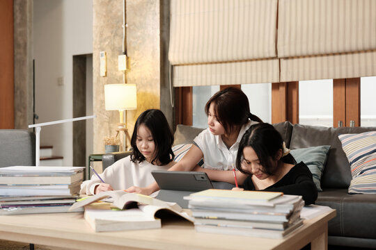 Three Asian teenage girls concentrate on online class, remote learning at home using tablet, writing and reading textbooks, self-study for back-to-school, Homeschooling education homework lifestyle.