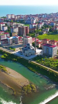 Vertical video. Ardeshen, Turkey. Ensar Mosque with twin minarets and large central dome, aerial view over the Firtina River estuary on a bright sunny morning with the Black Sea beyond. Aerial View, 