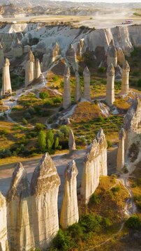 Vertical video. Goreme, Nevsehir, Turkey. Love Valley fairy chimneys, tall volcanic tuff pillars with dark basalt capstones, aerial view at golden hour over the eroded Cappadocian landscape. Aerial V