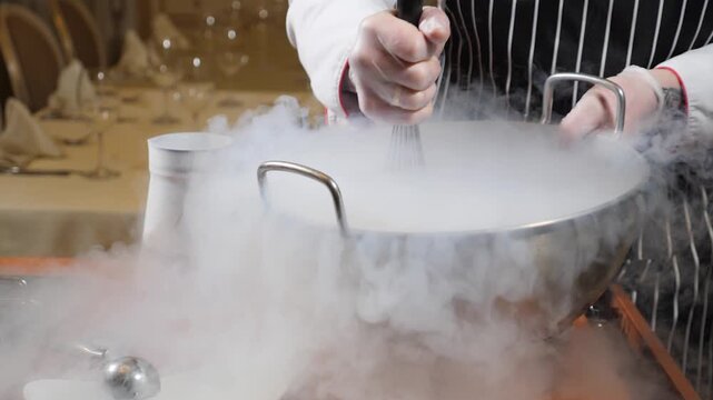 Chef whisking dessert mix in large metal bowl generating dense white liquid nitrogen smoke. Slow motion culinary show making artisan sorbet ice cream for elegant banquet dining 4k video