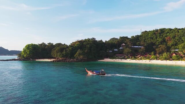 Stunning cinematic aerial, raditional longtail boat cruising through a tropical bay near the Phi Phi Islands, Krabi, Thailand, with turquoise water, sandy beach and lush island scenery