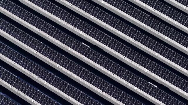 Rooftop photovoltaic arrays, Po Valley, Piacenza, Emilia-Romagna, Italy, revealing parallel solar panel rows, renewable energy infrastructure and geometric rooftop patterns, top-down drone forward fly