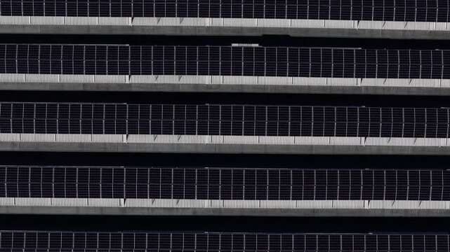 Rooftop photovoltaic arrays, Po Valley, Piacenza, Emilia-Romagna, Italy, revealing parallel PV rows, geometric rooftop design and grid-connected renewable electricity production, slow top-down drone